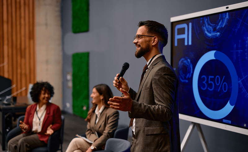 Man speaking at AI presentation with screen.